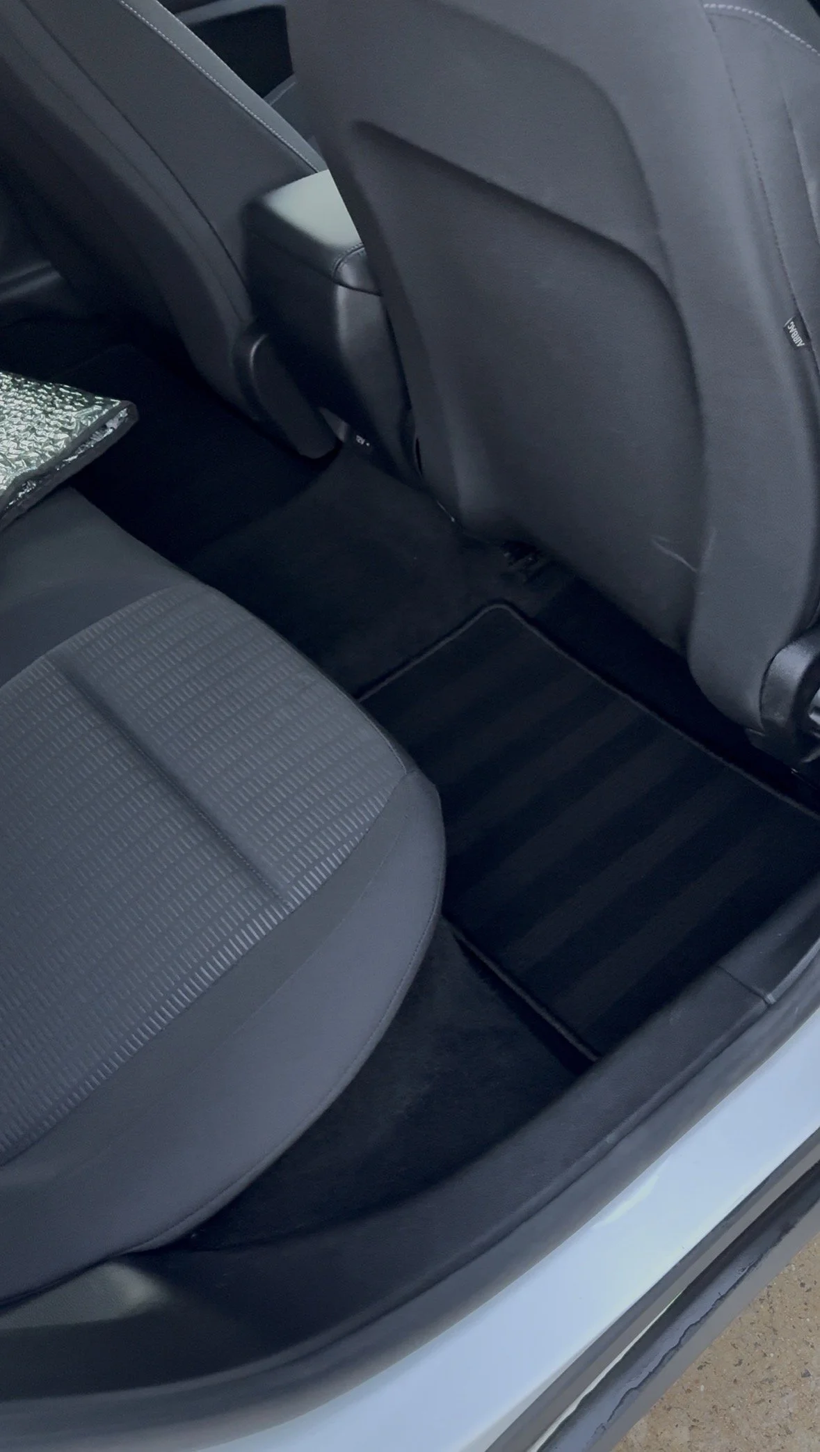 View of the back seat of a car, showing the fabric-covered seat and the rear of the front passenger seat with a small storage compartment and a patterned cloth item.