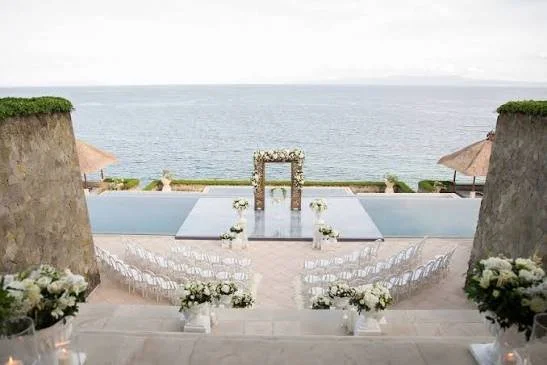 Beachside wedding setup with an aisle, floral arrangements, and an arch overlooking the ocean.