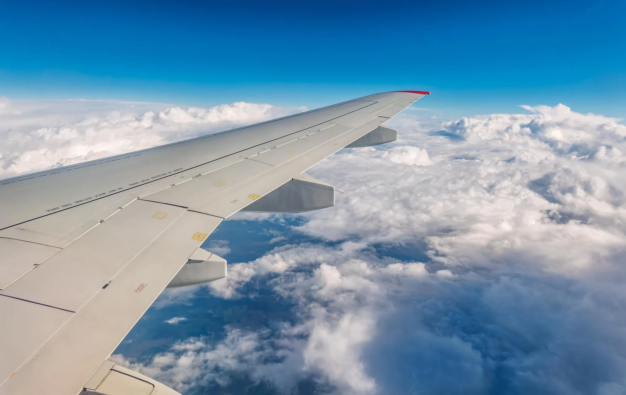 View of airplane wing above clouds with a blue sky.