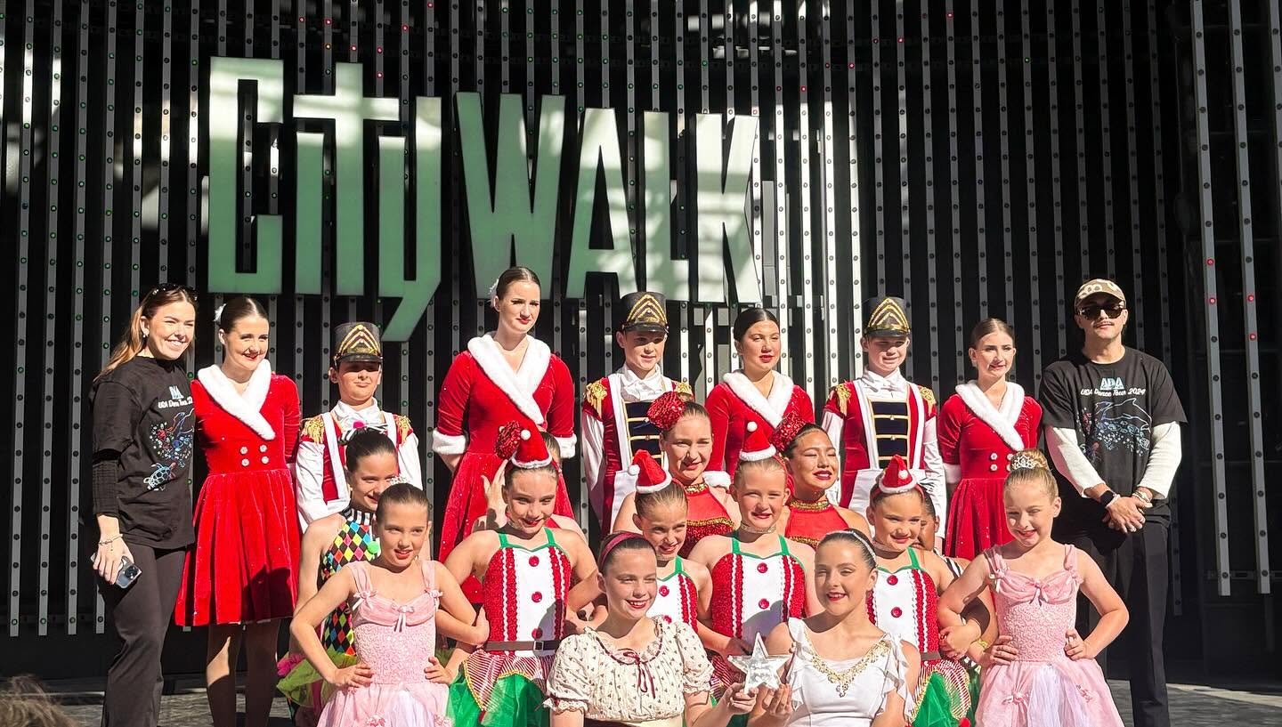 Group of young girls and women in colorful costumes at the Christmas City Walk event, posing on stage in front of a black backdrop with the word 'CITYWALK'.