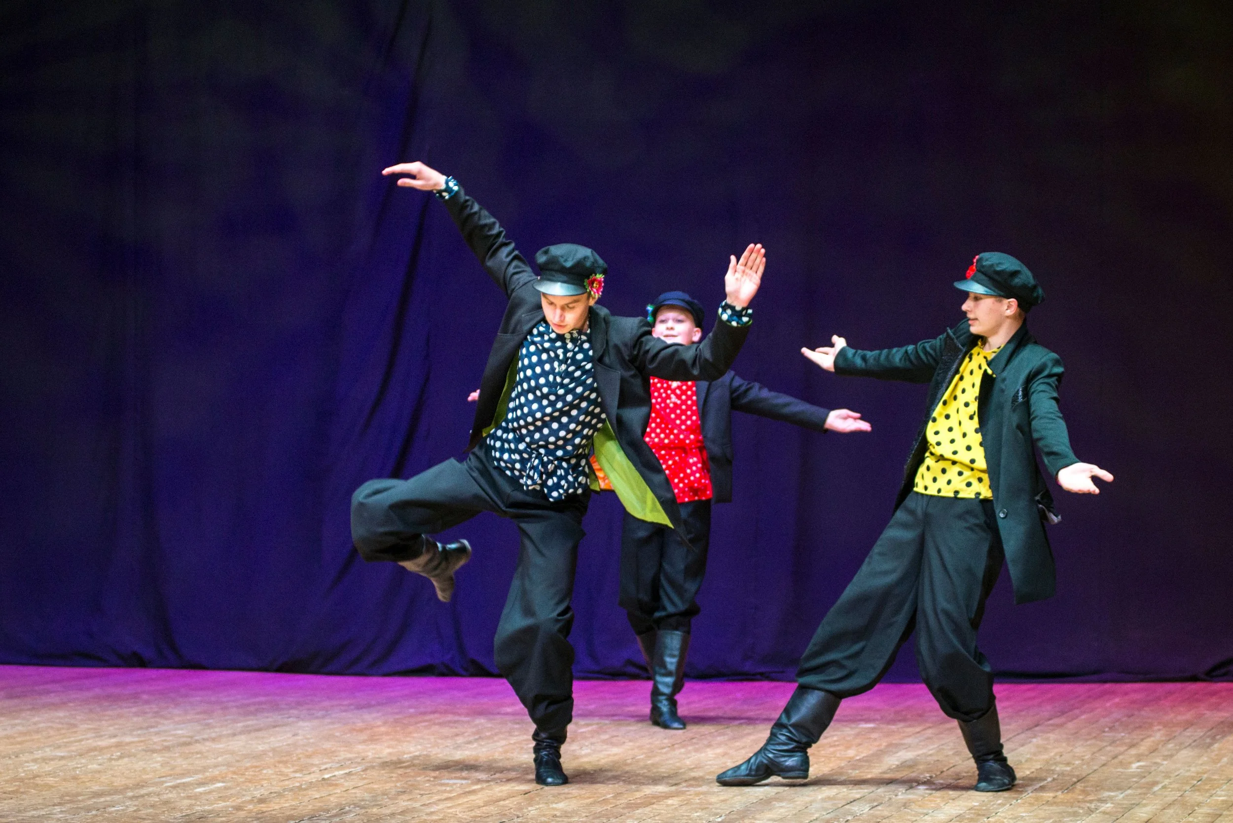 Three dancers in colorful costumes performing a traditional dance on stage with a dark background.