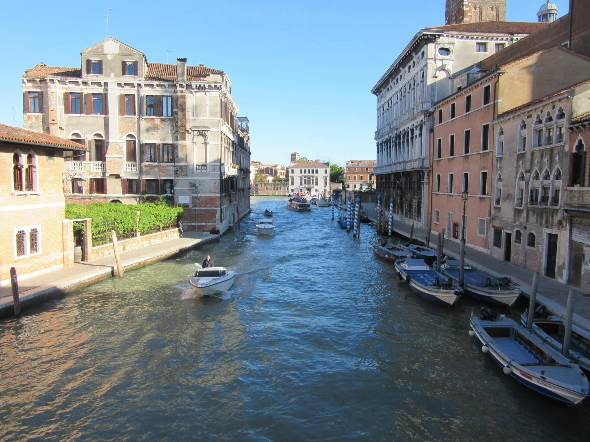 View of a canal in Venice, Italy, with historic buildings on both sides and boats on the water under a clear blue sky.