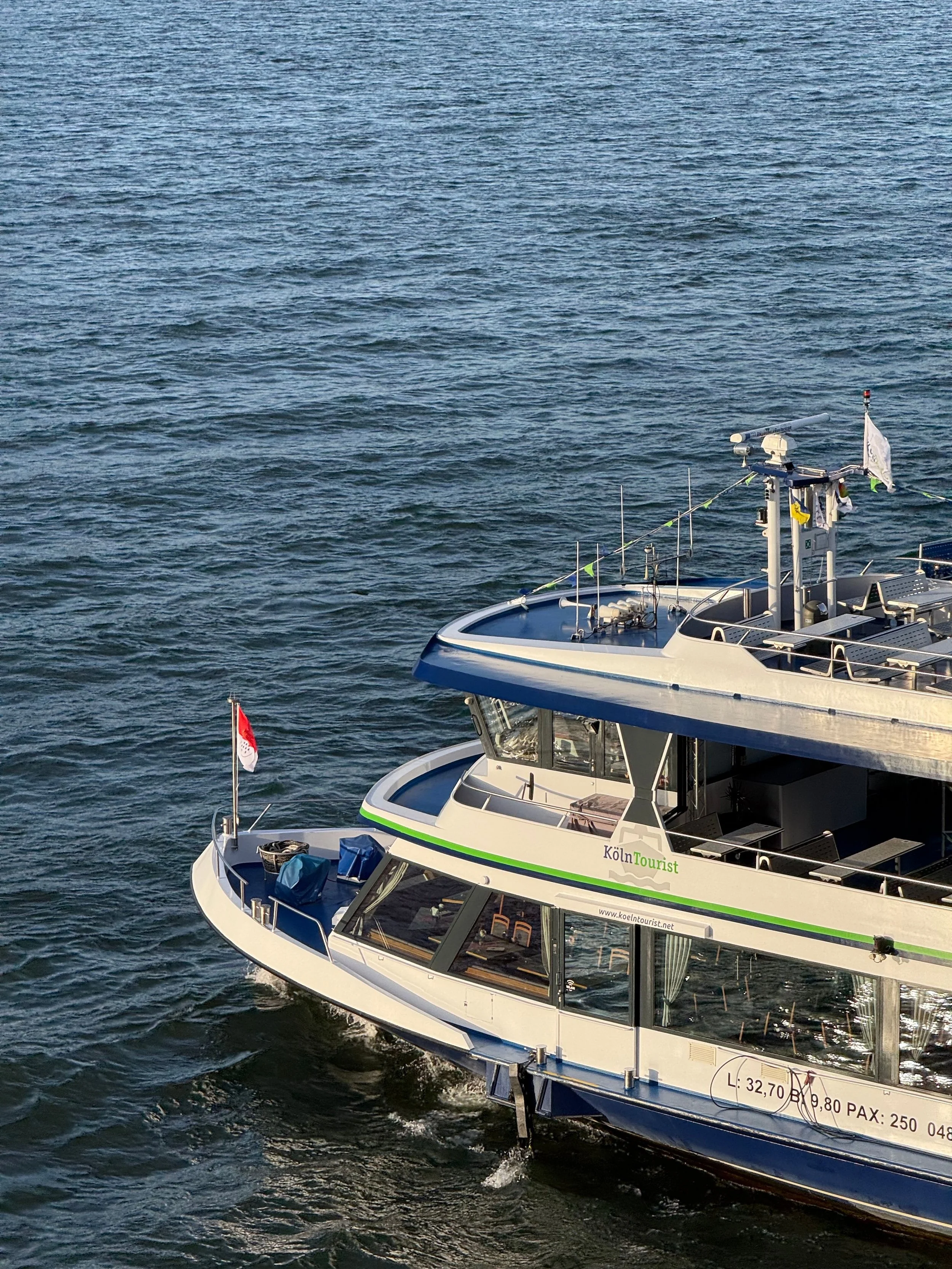 Luxury yacht on water with navigation equipment, flags, and a transparent deck area.