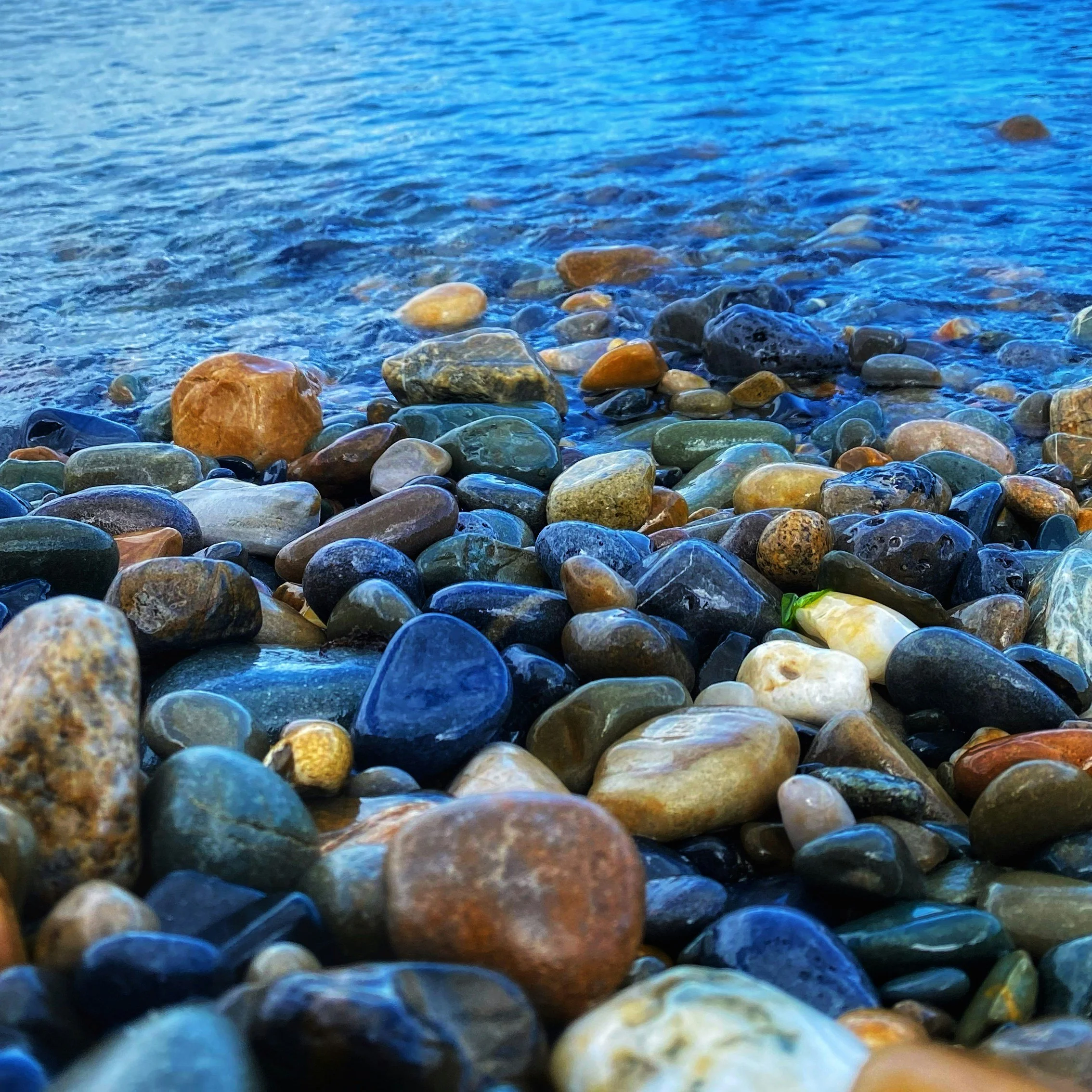Close-up view of multicolored smooth river stones along the shoreline with gentle water waves.