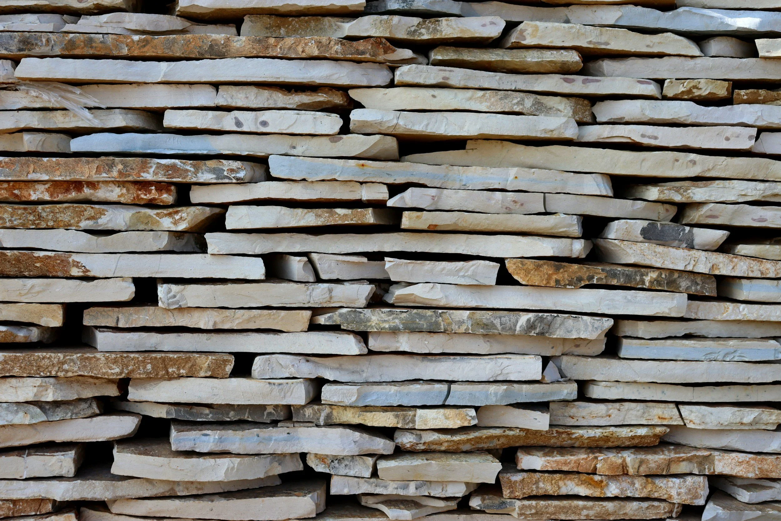 Stacked flat stone wall with various sizes and colors of beige, white, brown, and gray stones.