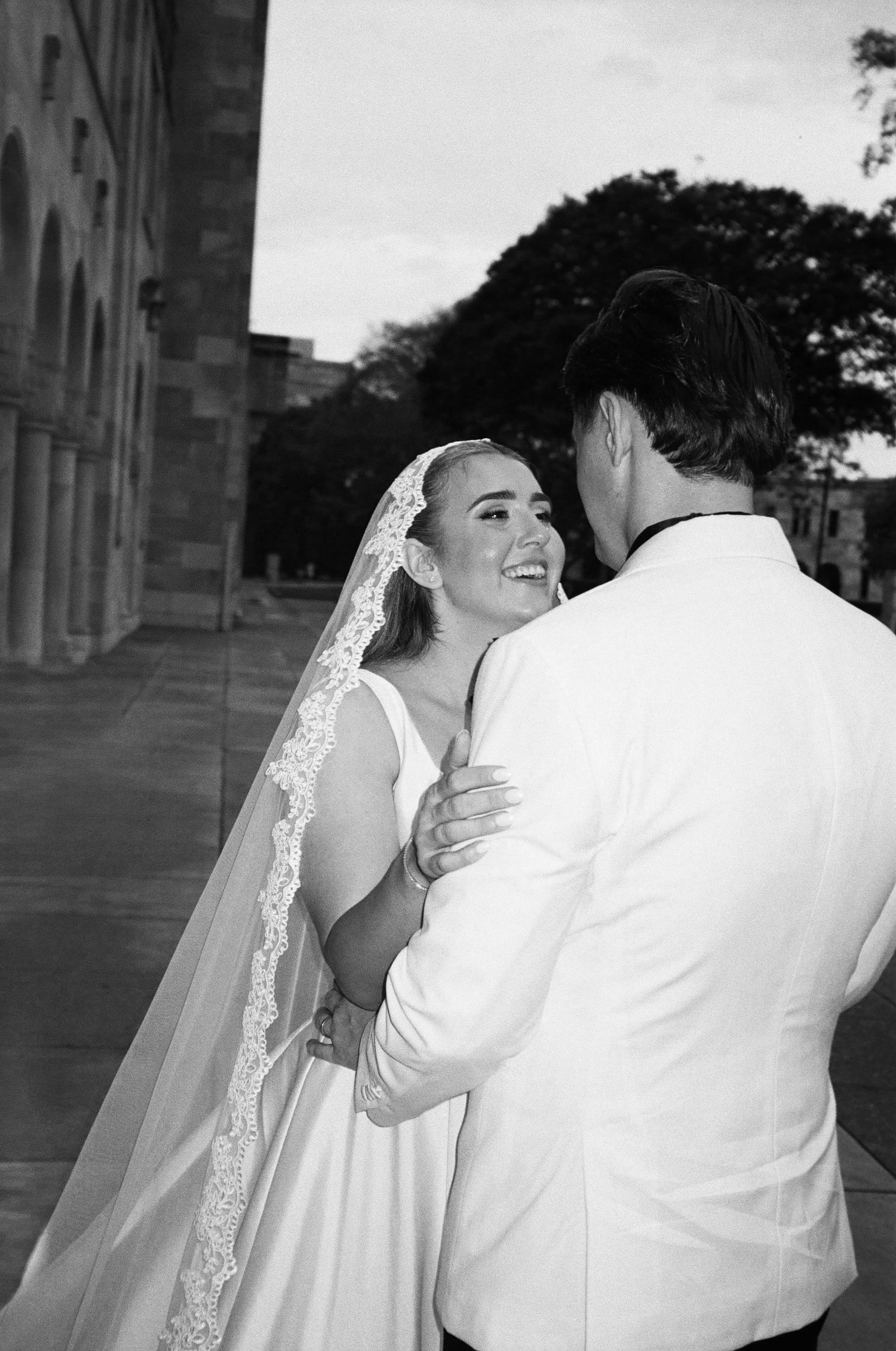 A bride and groom share a dance outdoors, smiling at each other during their wedding reception.