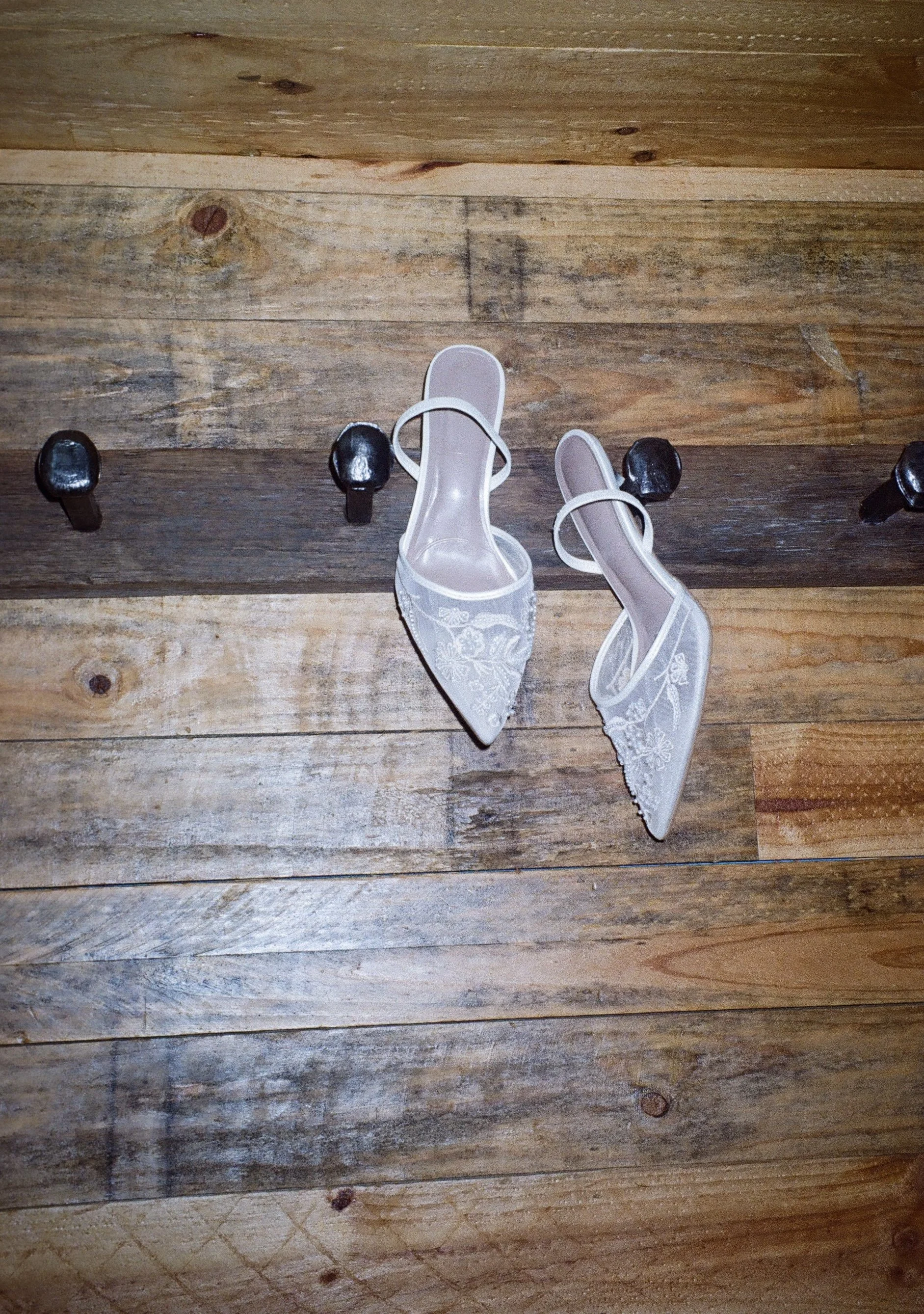 Pair of white lace high-heeled shoes on wooden floor.