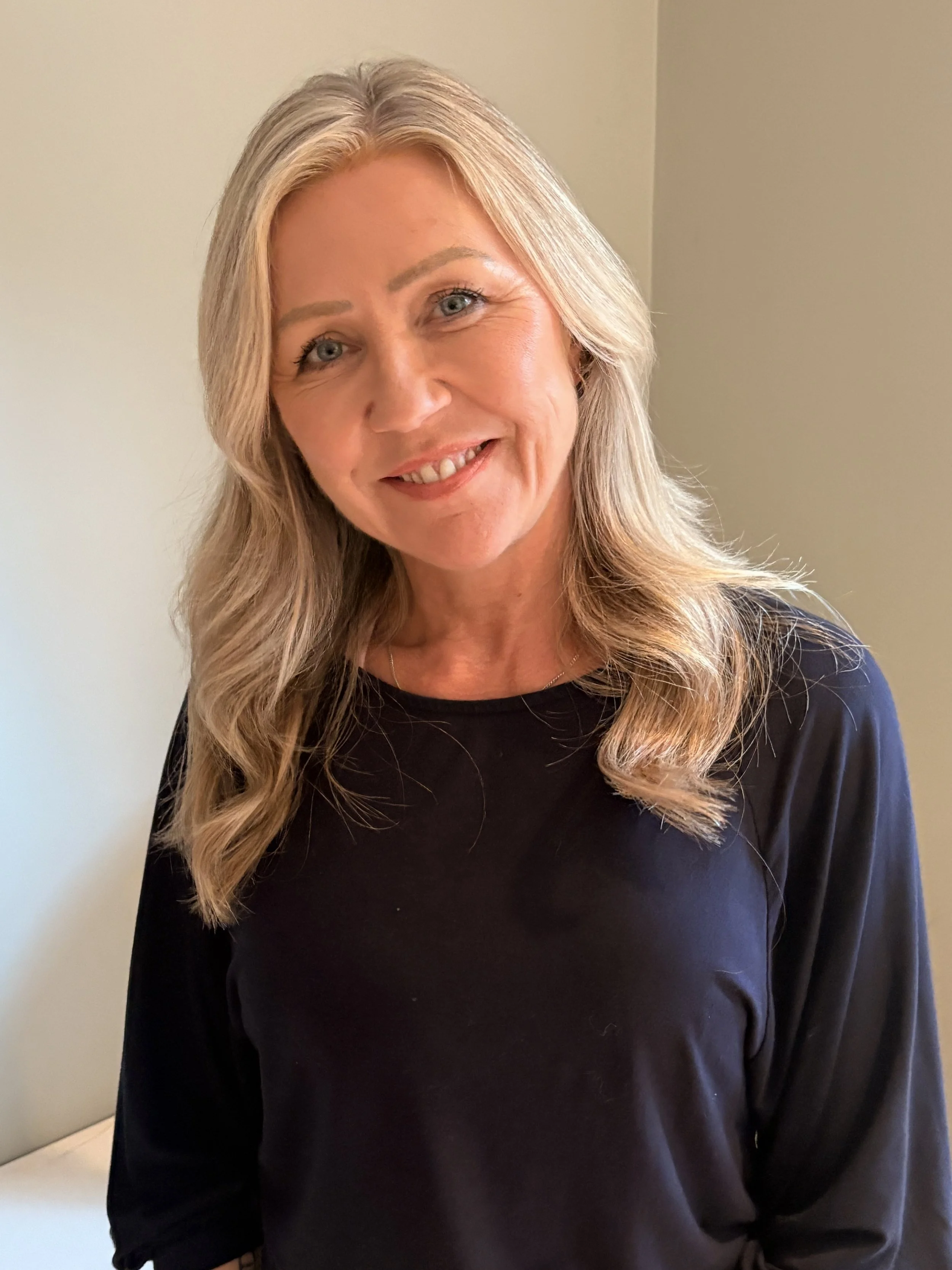 Jane Wrafter Muswell Hill Therapy with long blonde hair wearing a black top standing against a beige wall.