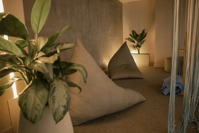 Bedroom with large bed, gray pillows, potted plants, beige walls, and soft lighting.