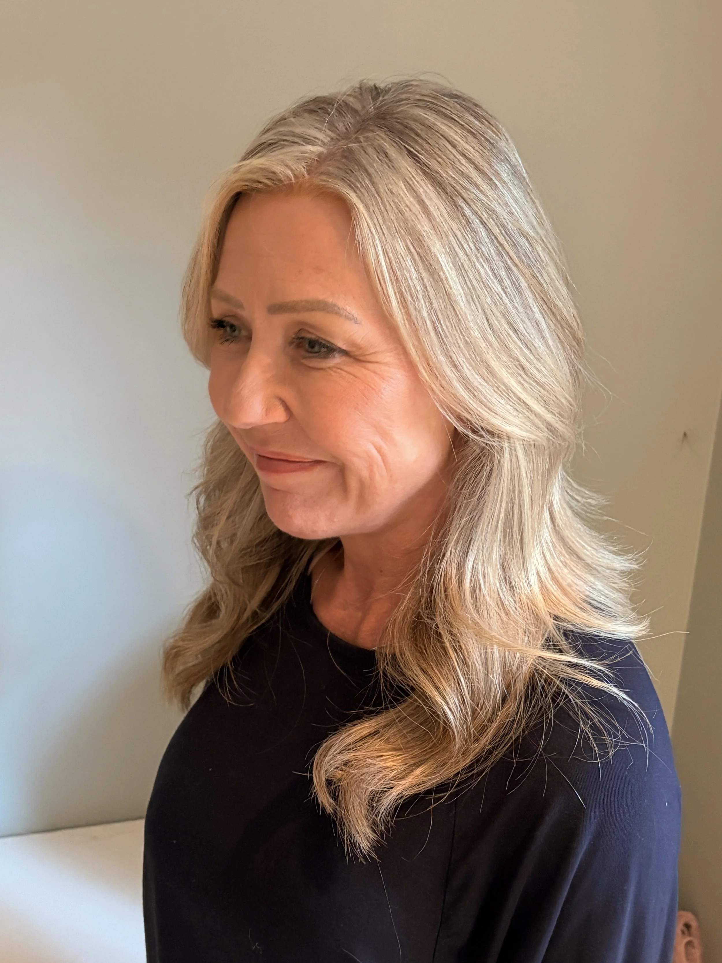 Jane Wrafter Muswell Hill Therapy face with blonde hair styled in loose waves, wearing a black top, standing against a plain light-colored wall.