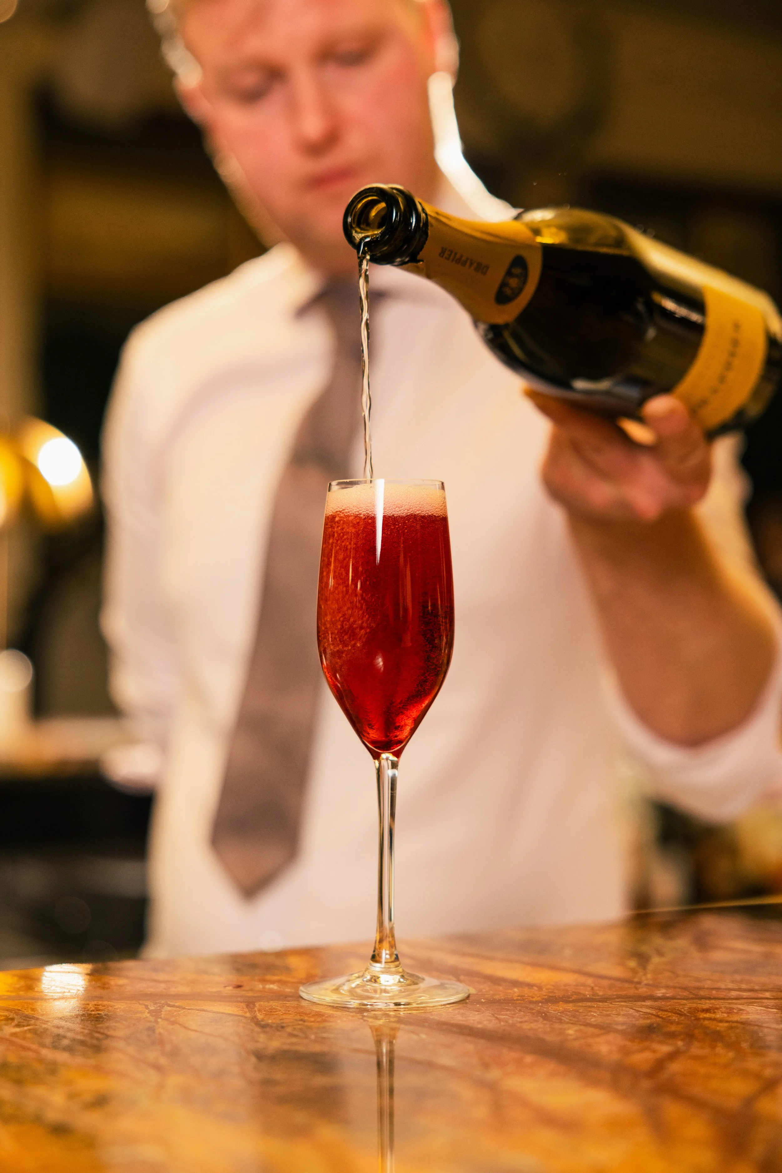 Man pouring champagne into a glass with a blurred background.