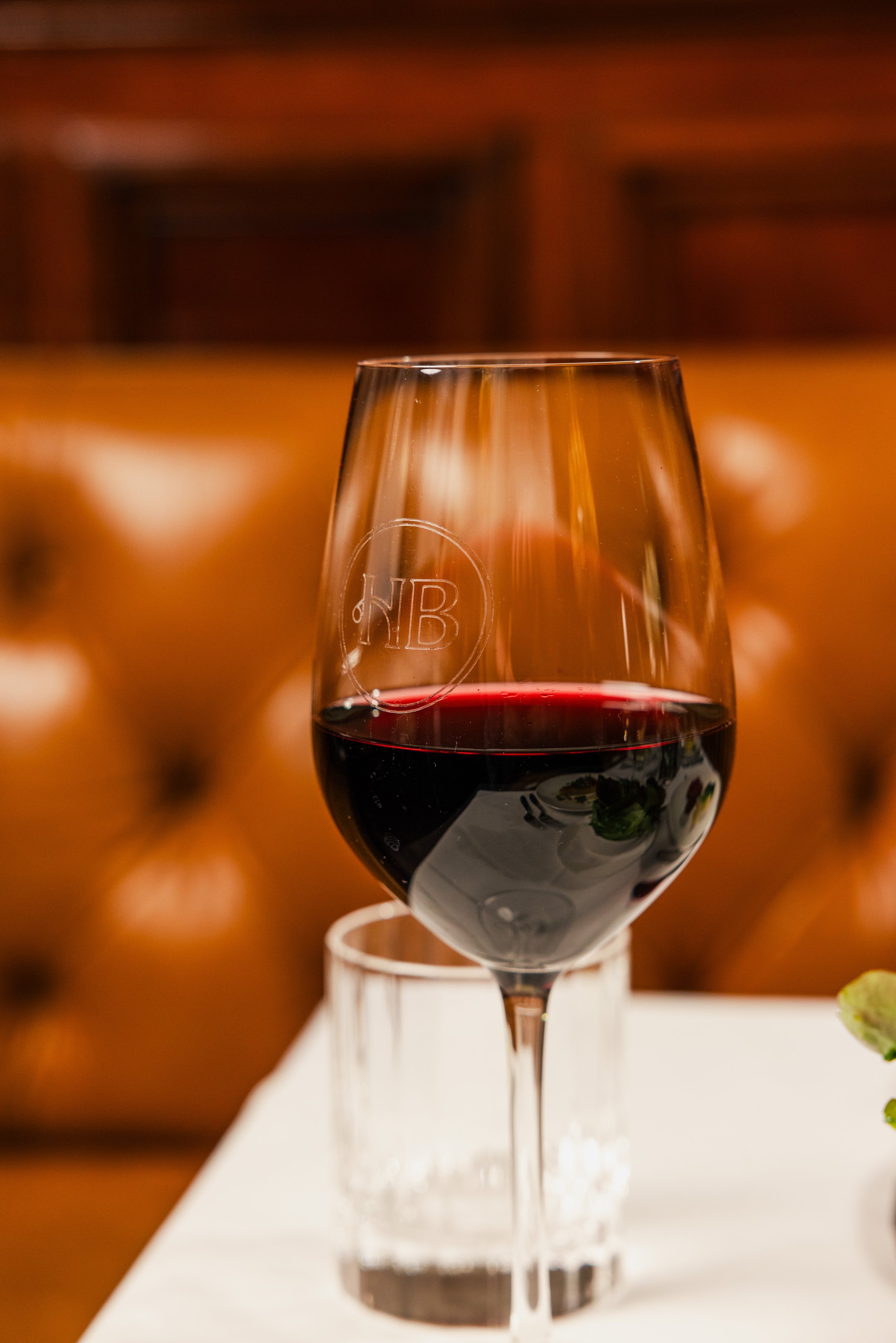 A glass of red wine on a white surface with out-of-focus background featuring warm brown tones.