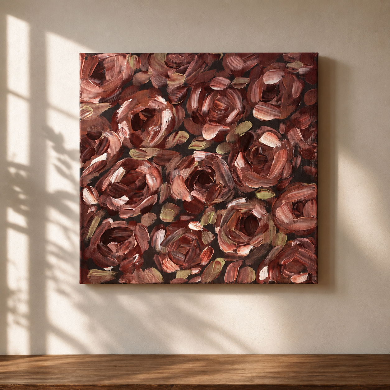A square canvas painting of abstract roses in shades of dark red, pink, and green, hanging on a beige wall in a room with wooden flooring and sunlight casting shadows.