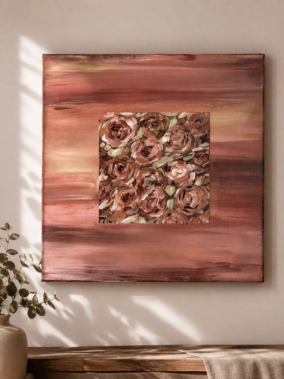 Square painting with pink, brown, and beige abstract floral design, mounted on a large pink wooden panel, with a pot of green leafy plant to the left and a beige cloth on a wooden surface.