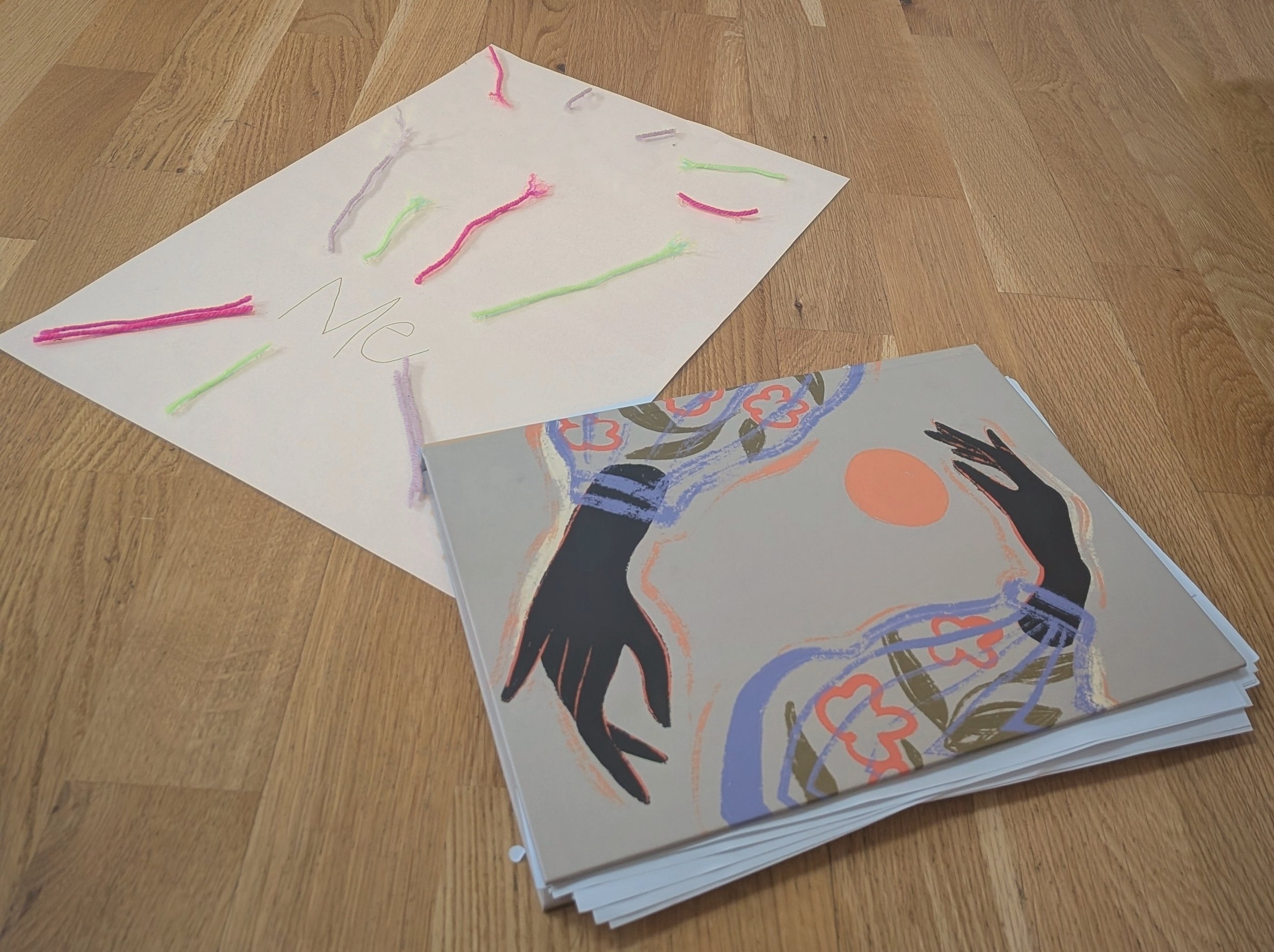 A stack of papers with colorful abstract artwork and drawings, placed on a wooden floor.