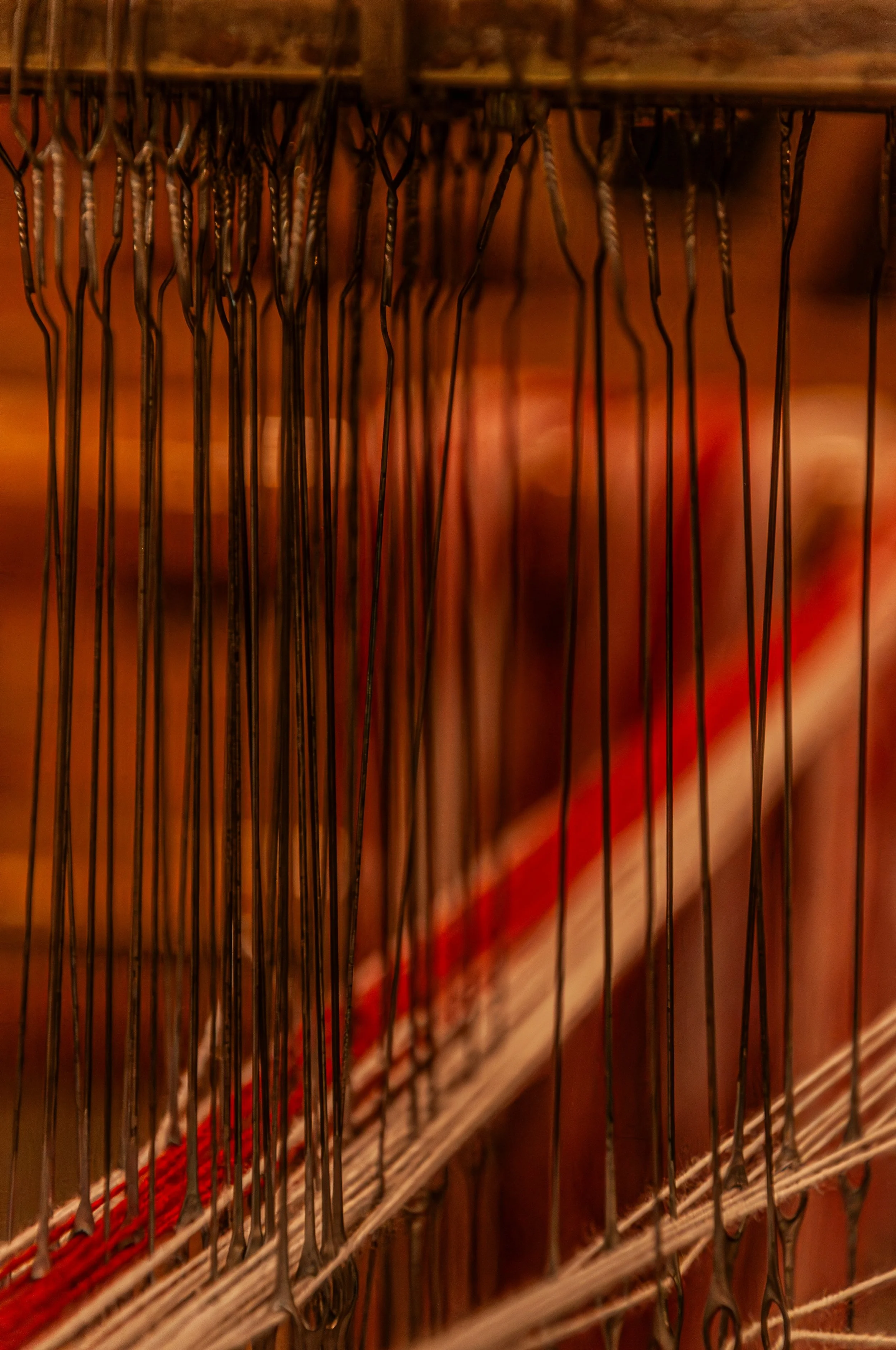 Close-up of a vintage wire letterpress printing press with metal type arranged on a composing stick, featuring a red and beige printed line visible in the background.