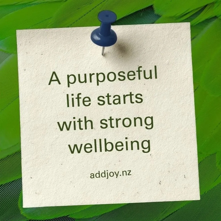 Note pinned to a green feather background with the quote 'A purposeful life starts with strong wellbeing' and a website link www.addjoy.nz