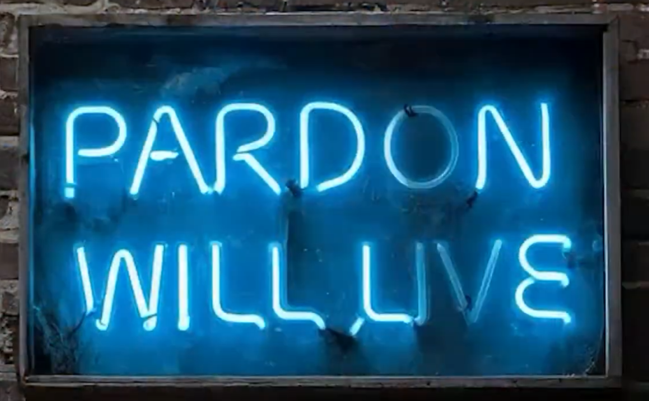 Neon sign that reads 'Pardon Will Live' in blue lettering, mounted on a brick wall.