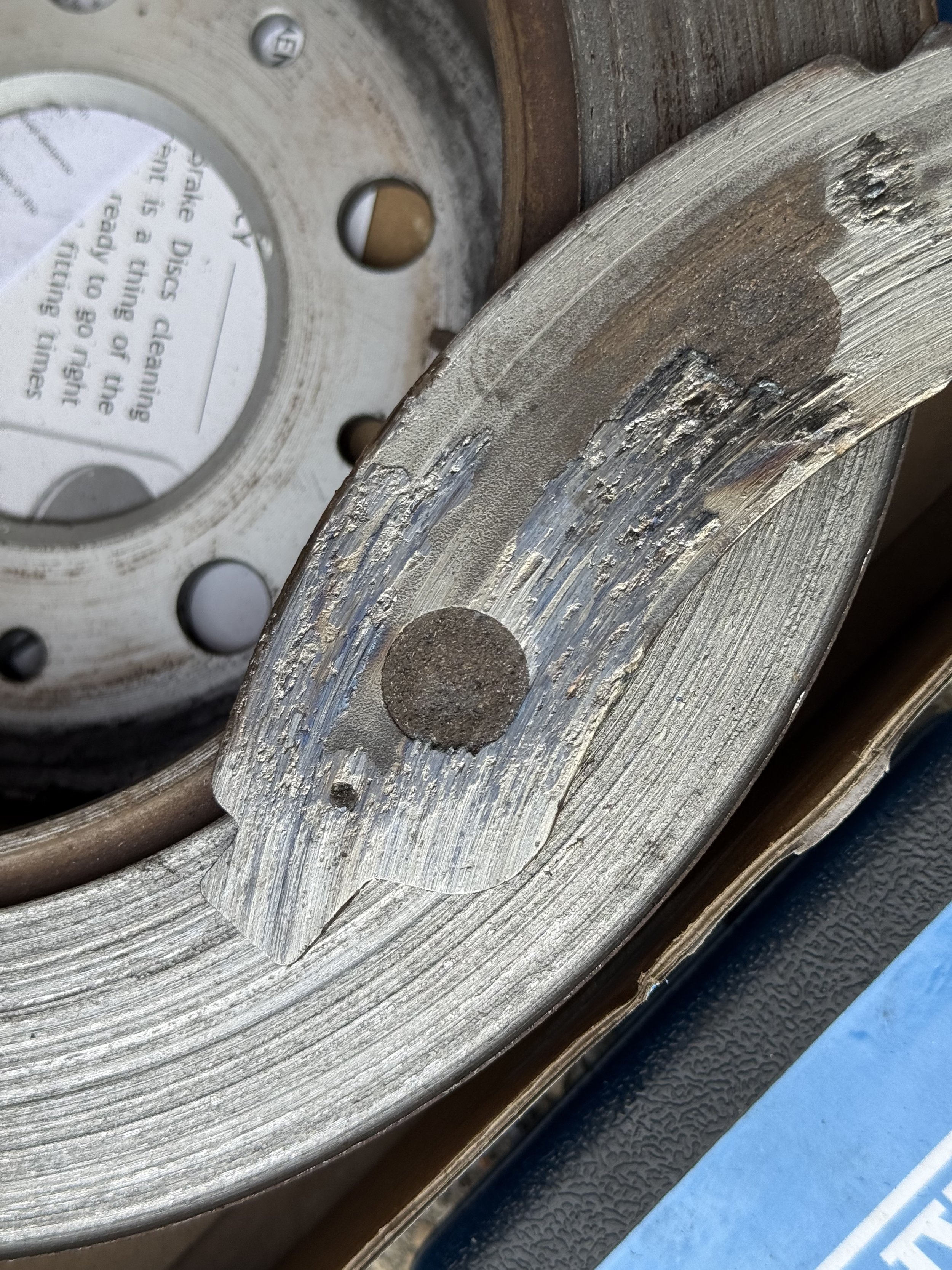 Close-up of a metallic mechanical part with a circular component, visible screws, and textured surface, with a piece of blue equipment in the background.