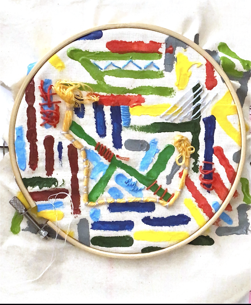 Embroidery hoop holding fabric painted with colourful brushstrokes and stitched with yarn in red, yellow and blue thread.