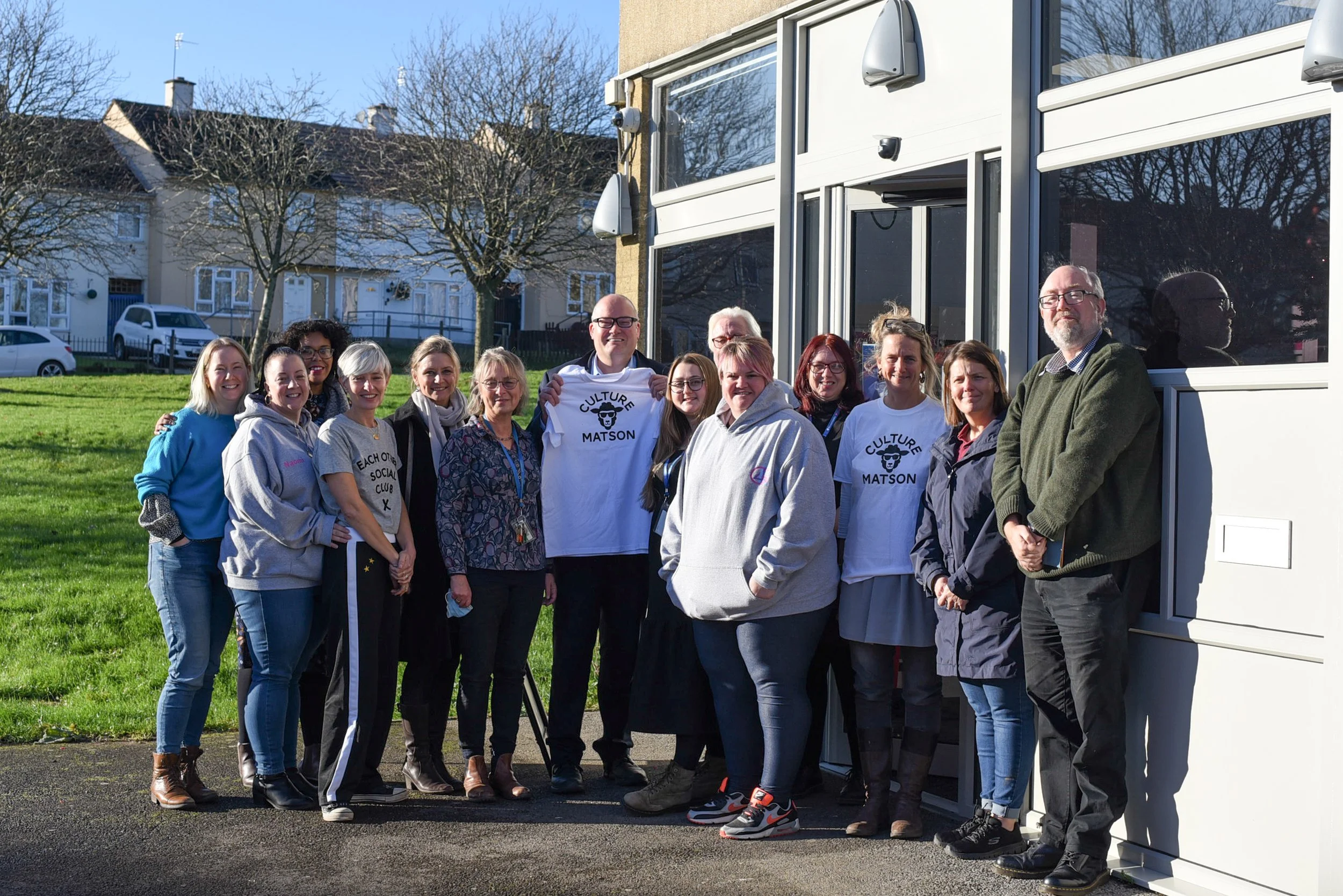 Darren Henley and team standing outside Matson library holding a white t-shirt with Culture Matson. Photo by Rebecca Boseley