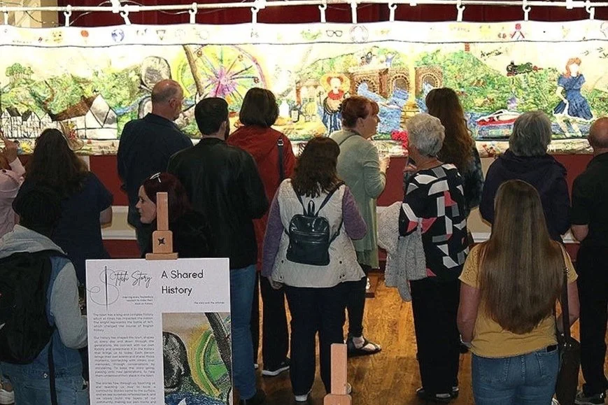 A group of people looking at a tapestry.