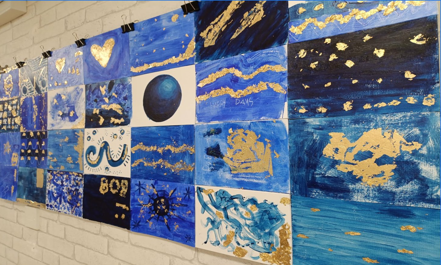 Multiple blue and gold artworks displayed on a white brick wall