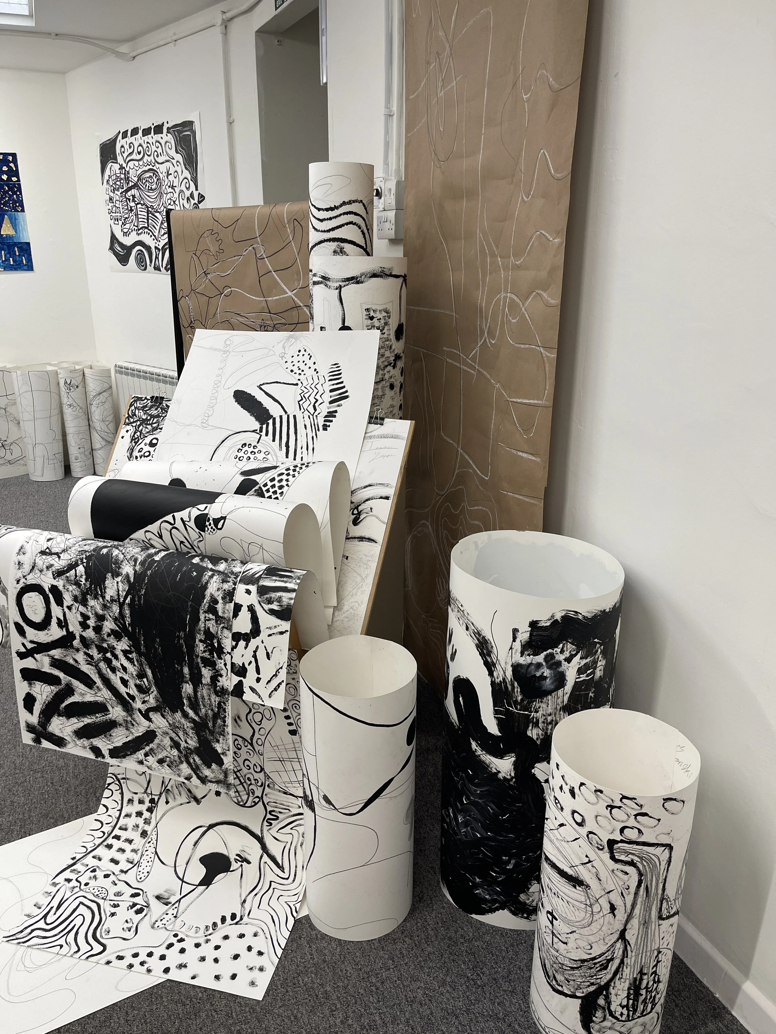 Black ink abstract drawings on large sheets of white and brown paper in a room with white walls.