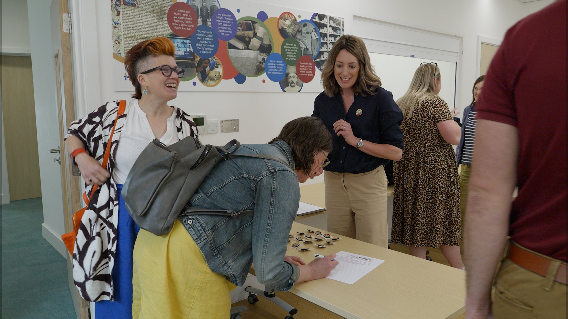 Attendees sign in at a registration table at a Create Glos event, with a woman smiling beside them.