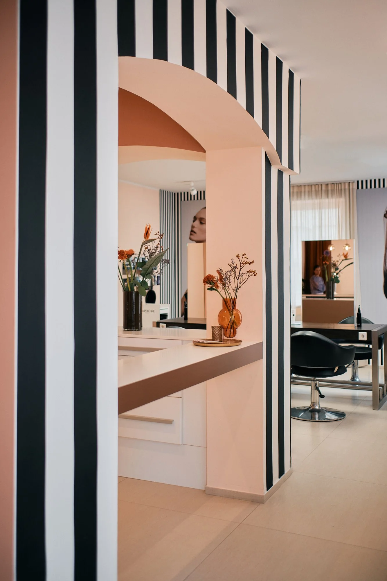 Innenansicht eines modernen Friseursalons mit schwarzem und weißem Streifenmuster an den Wänden, Blumen in Vasen und einem Maske am Spiegel.