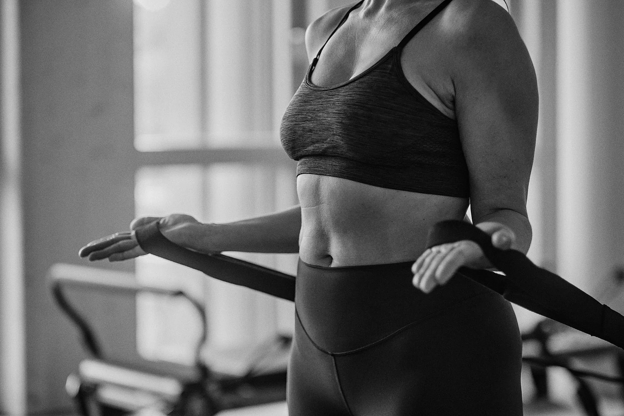 Frau im Sportoutfit bei Yoga, die mit einem Yoga-Block in den Händen steht, im Fitnessstudio, schwarz-weiß Foto.