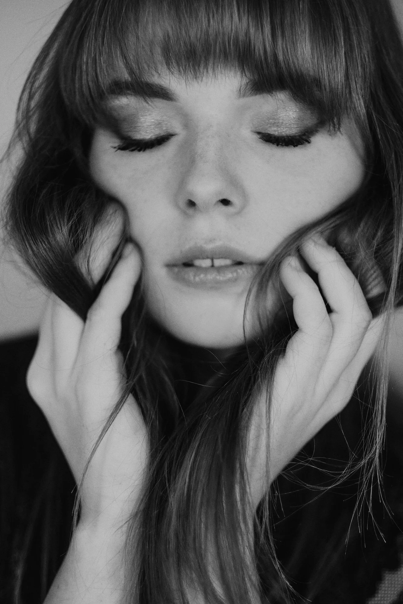Schwarz-weiß-Fotografie eines nahen Porträts einer Frau mit geschlossenen Augen und langen Haaren, die zart ihr Gesicht berühren.