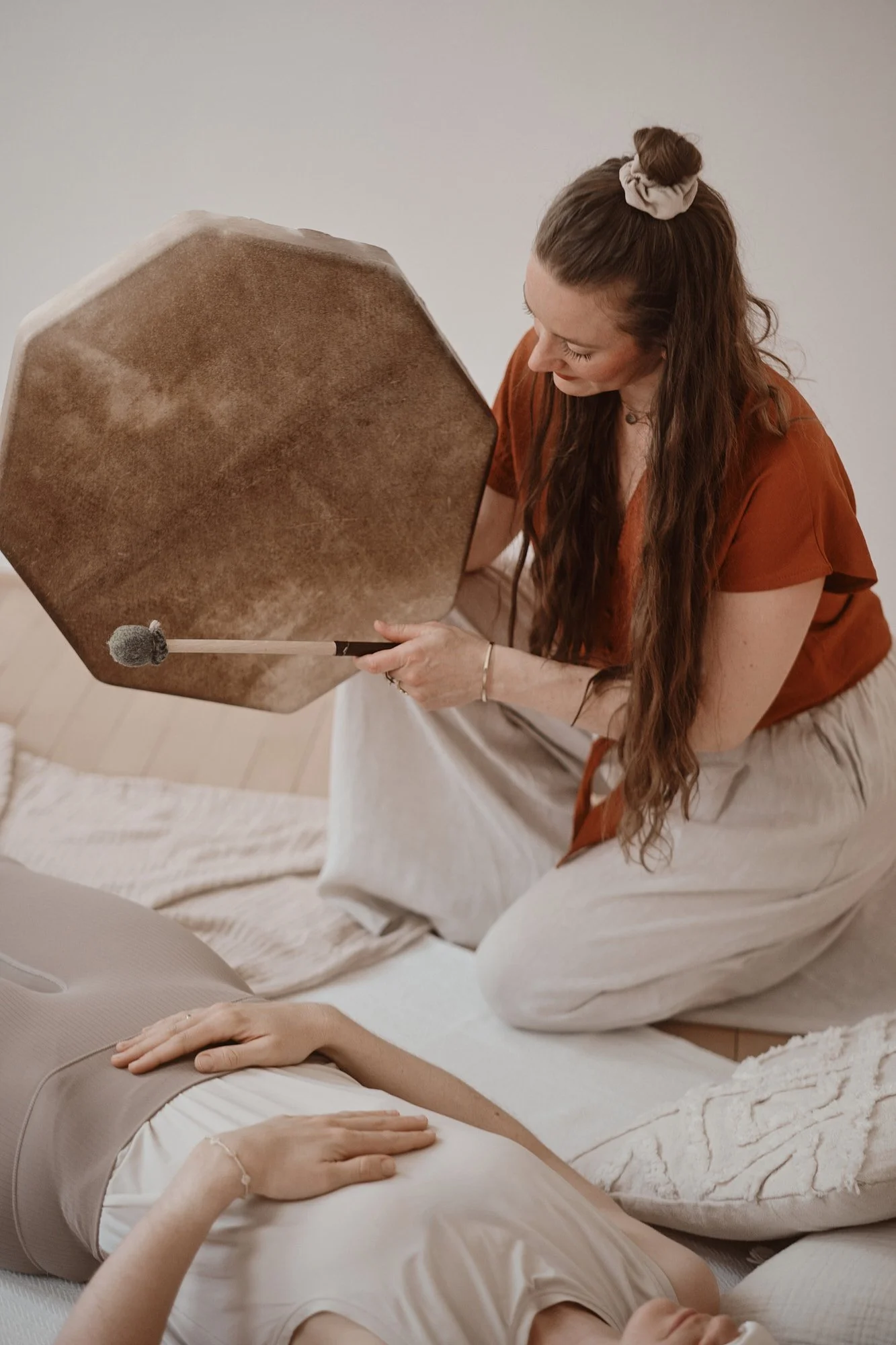 Eine Frau macht eine Klangschalenmassage bei einer Person, die auf dem Boden liegt.