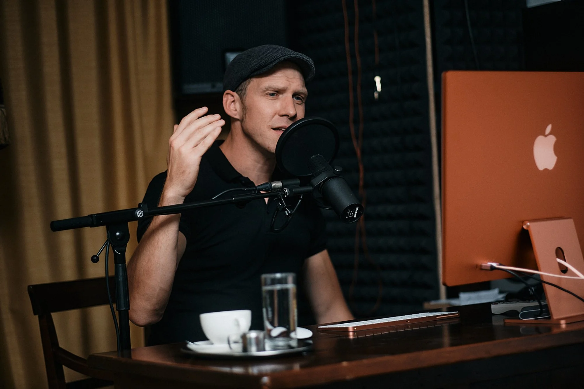 Ein Mann trägt eine Mütze und spricht in einem Tonstudio mit einem Mikrofon.