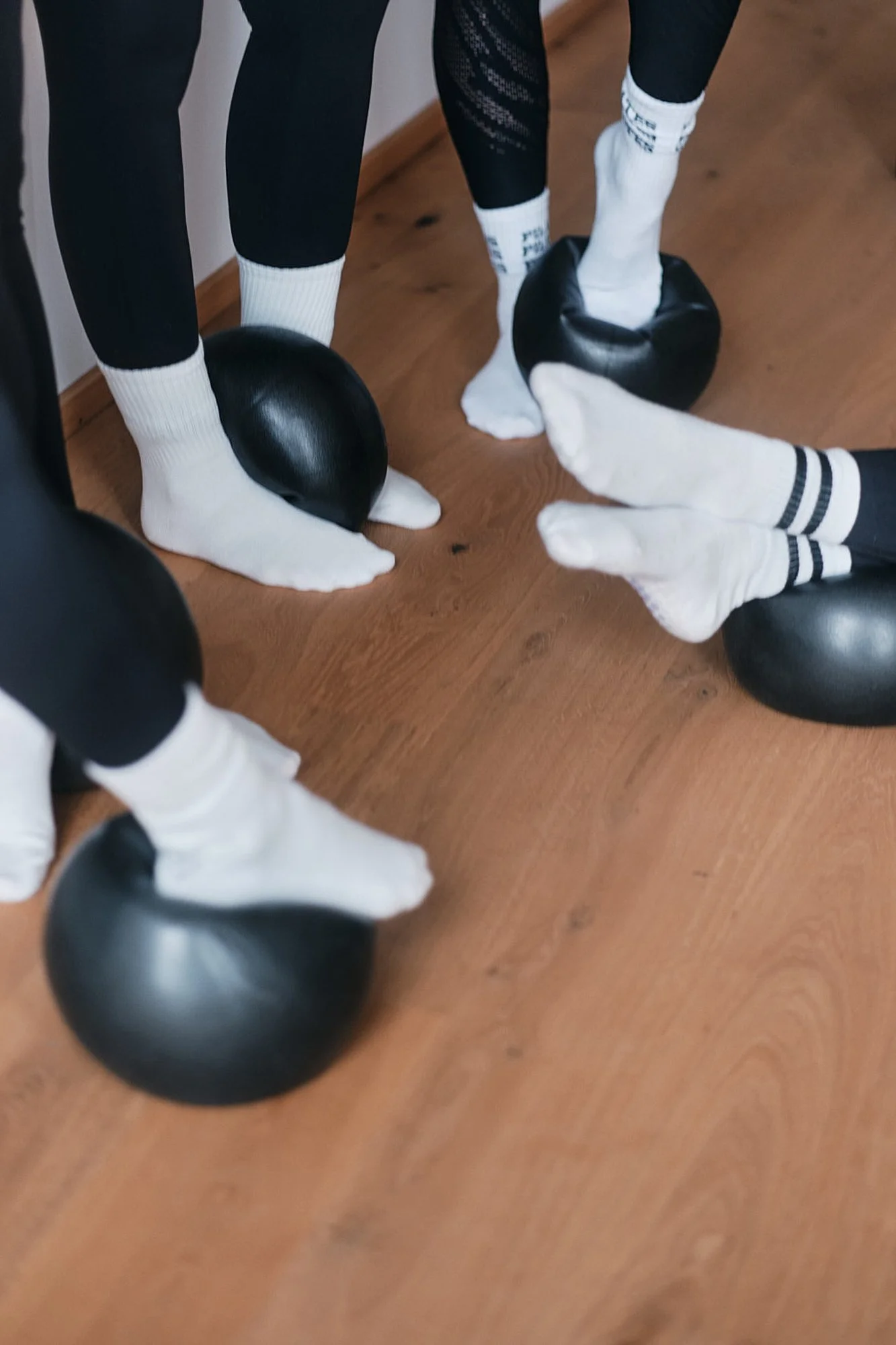 Zwei Figuren mit schwarzen Ballhüllen, weißen Socken und schwarzen Kleidungsstücken stehen auf einem Holzboden, während eine Person sie berührt.