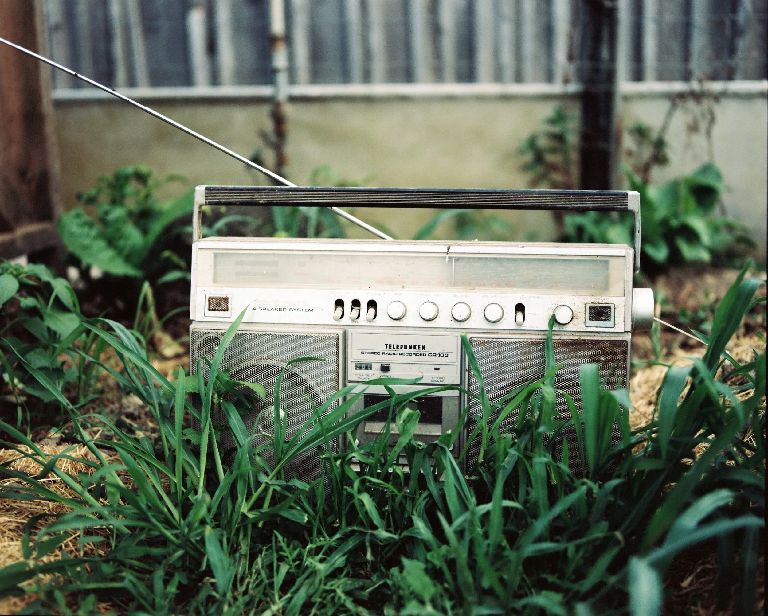 Ein altes Stereo-Radiorekorder steht im Garten, umgeben von grünem Gras und Pflanzen.