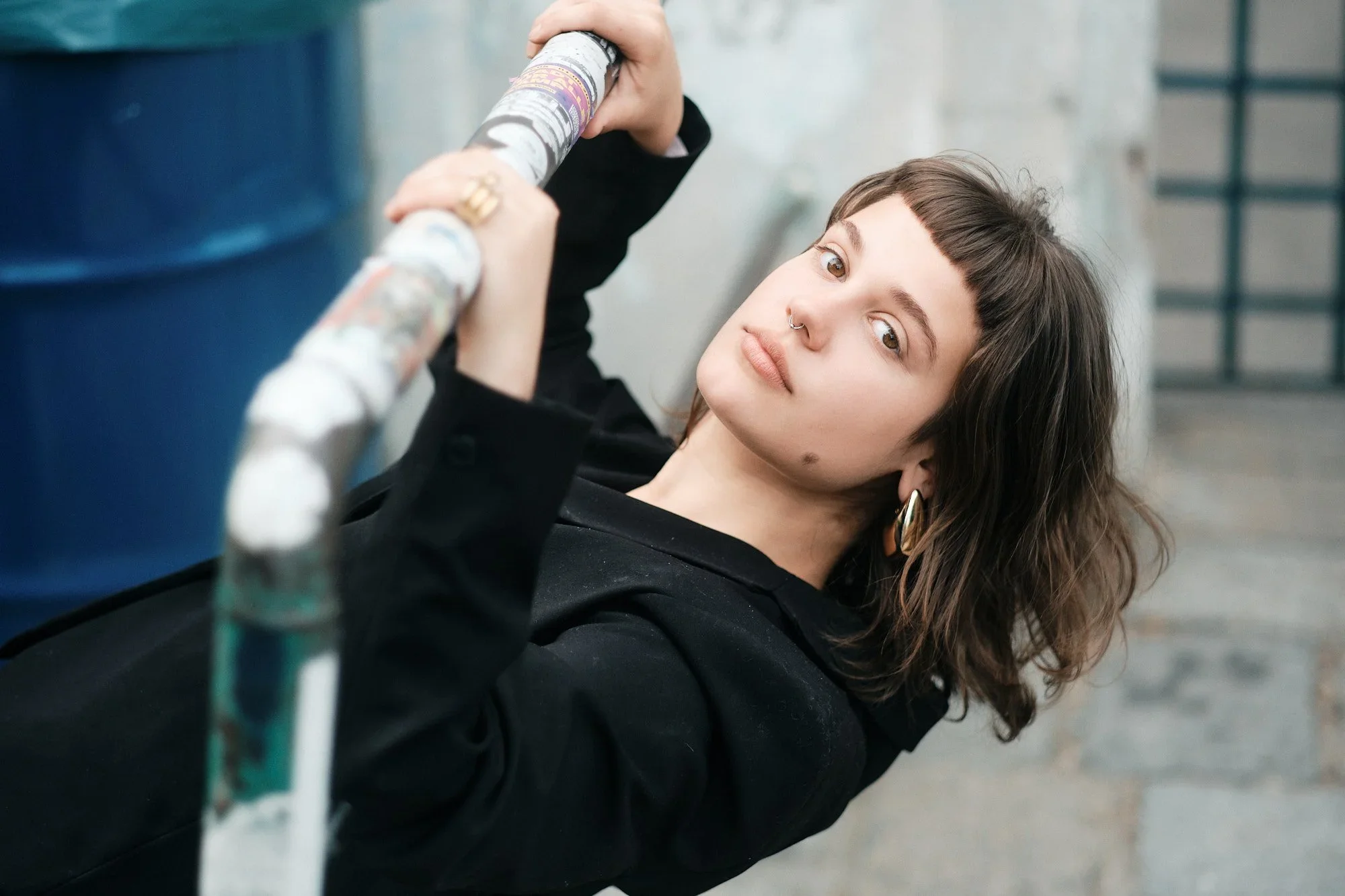 Eine junge Frau mit dunklen Haaren, piercing in der Nase und Ohrringen liegt auf dem Boden und hält eine Wasserflasche in der Hand, während sie auf den Boden schaut.