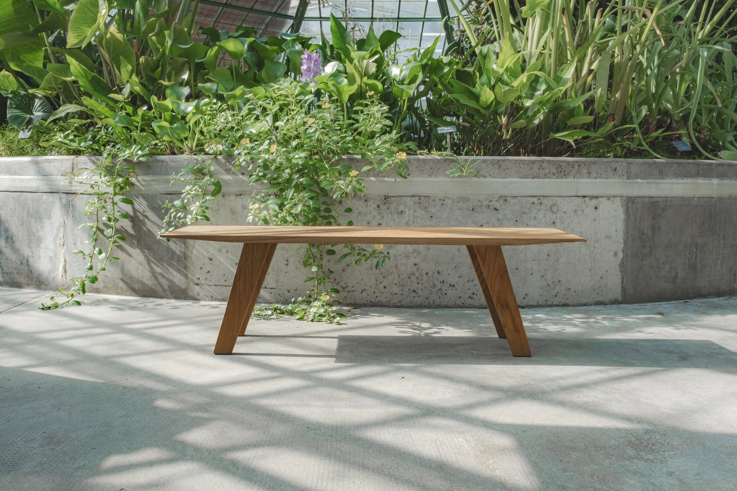 Handmade wooden bench crafted from solid oak wood with a natural finish standing in front of green botanical garden scenery.
