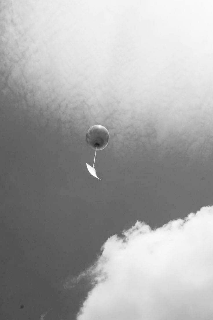 A hot air balloon floating in the sky next to clouds, captured in black and white.