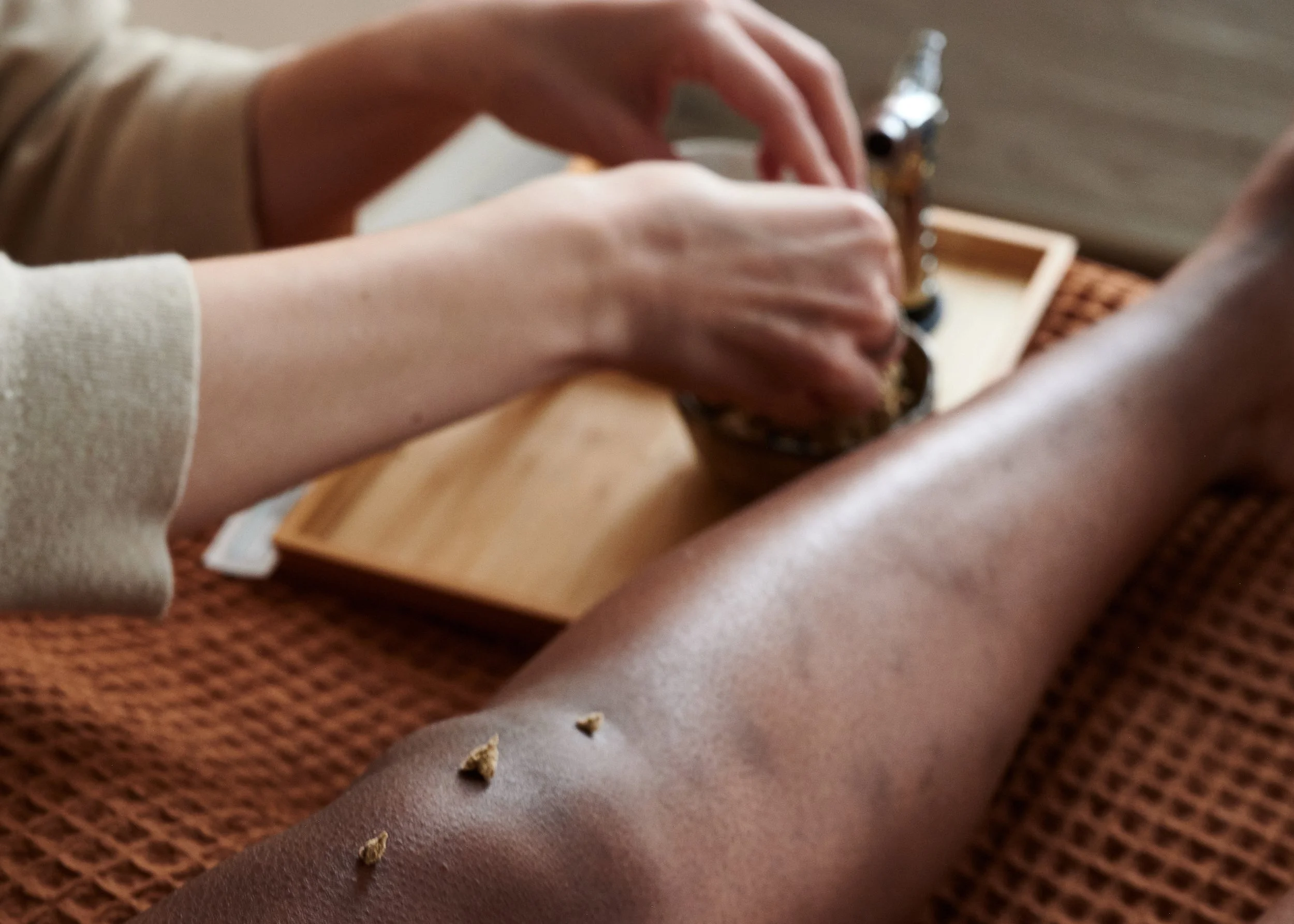 Close-up of a person's hands playing a small wooden musical instrument, possibly a kalimba, on a brown textured surface with some scattered crumbs.