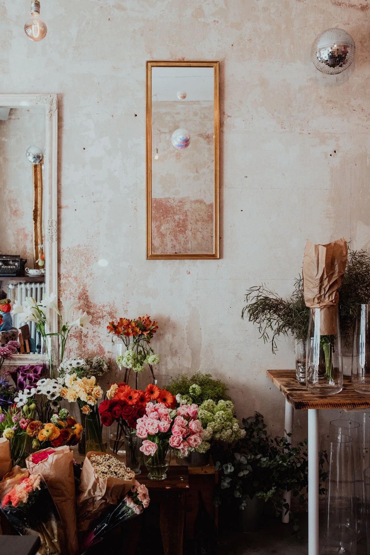 Colorful flower shop interior with bouquets of fresh flowers, vintage mirrors, exposed textured walls, and a hanging disco ball