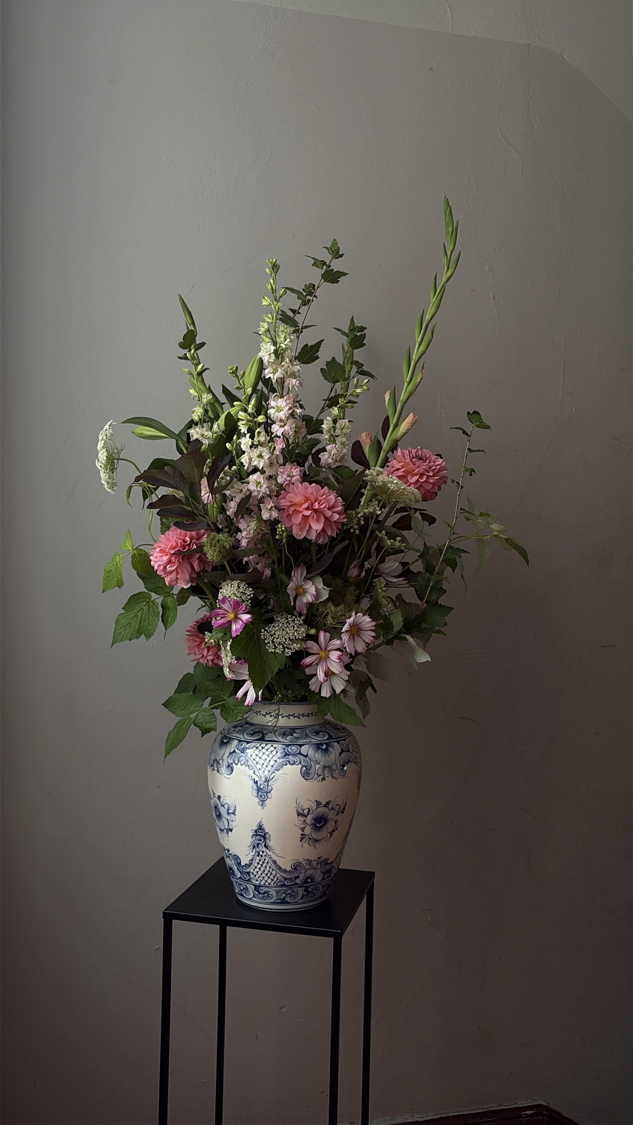 Lush pink and white flower arrangement in a blue-and-white ceramic vase on a black pedestal table