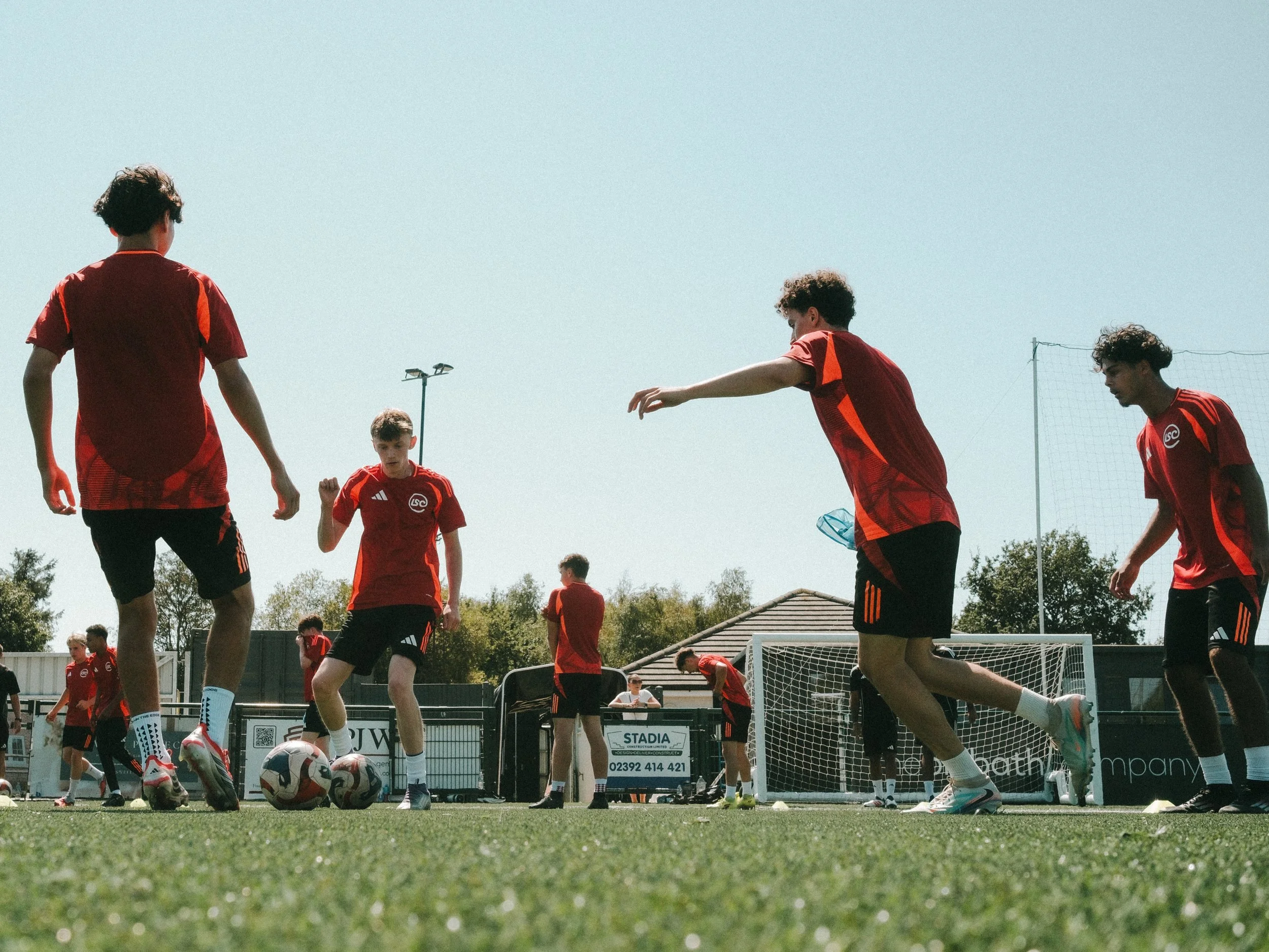 A group of young male soccer players in red jerseys practicing or warming up on a soccer field under a clear sky.