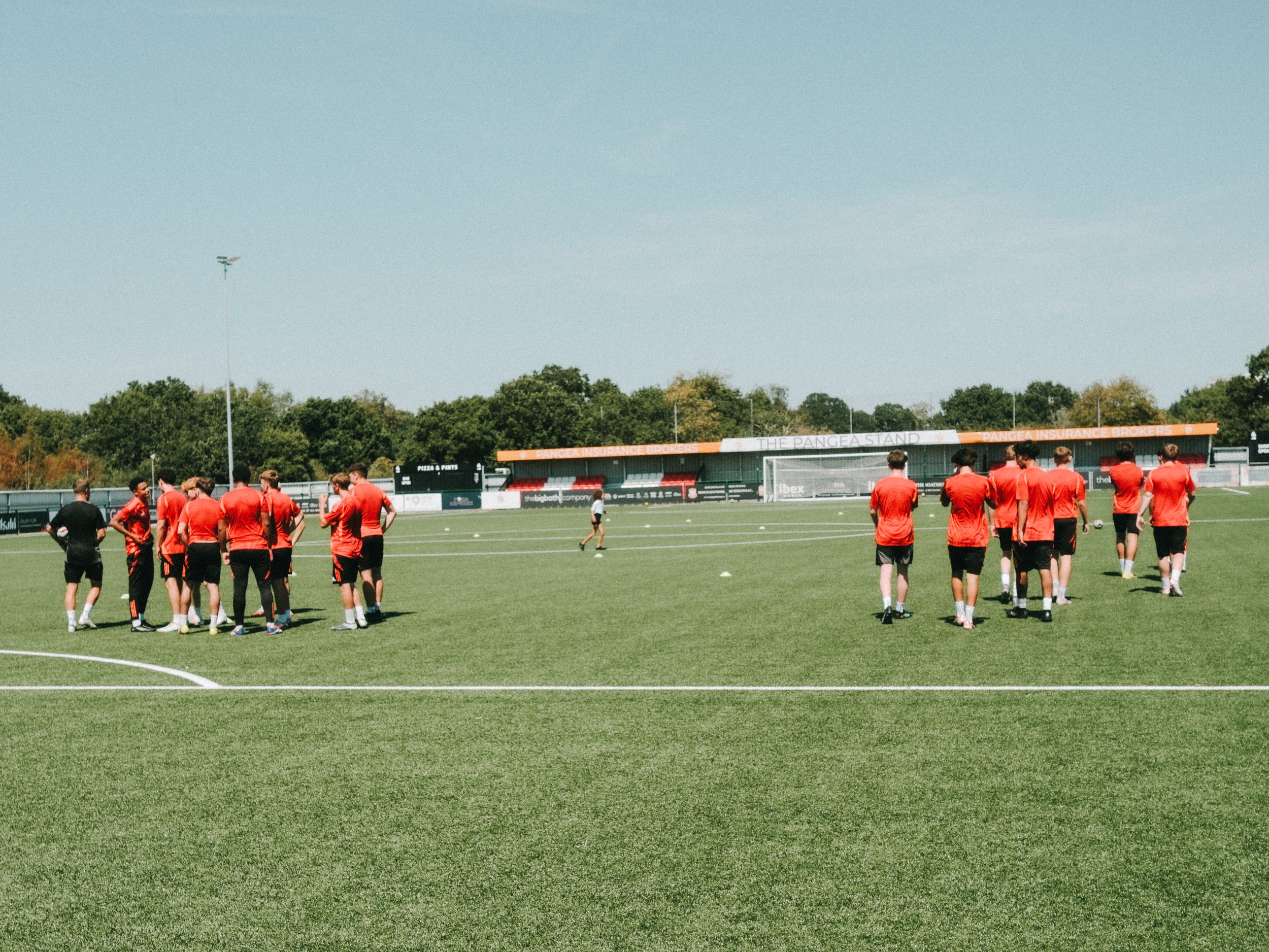 Soccer team in red jerseys standing on a soccer field during practice or training session under clear skies.
