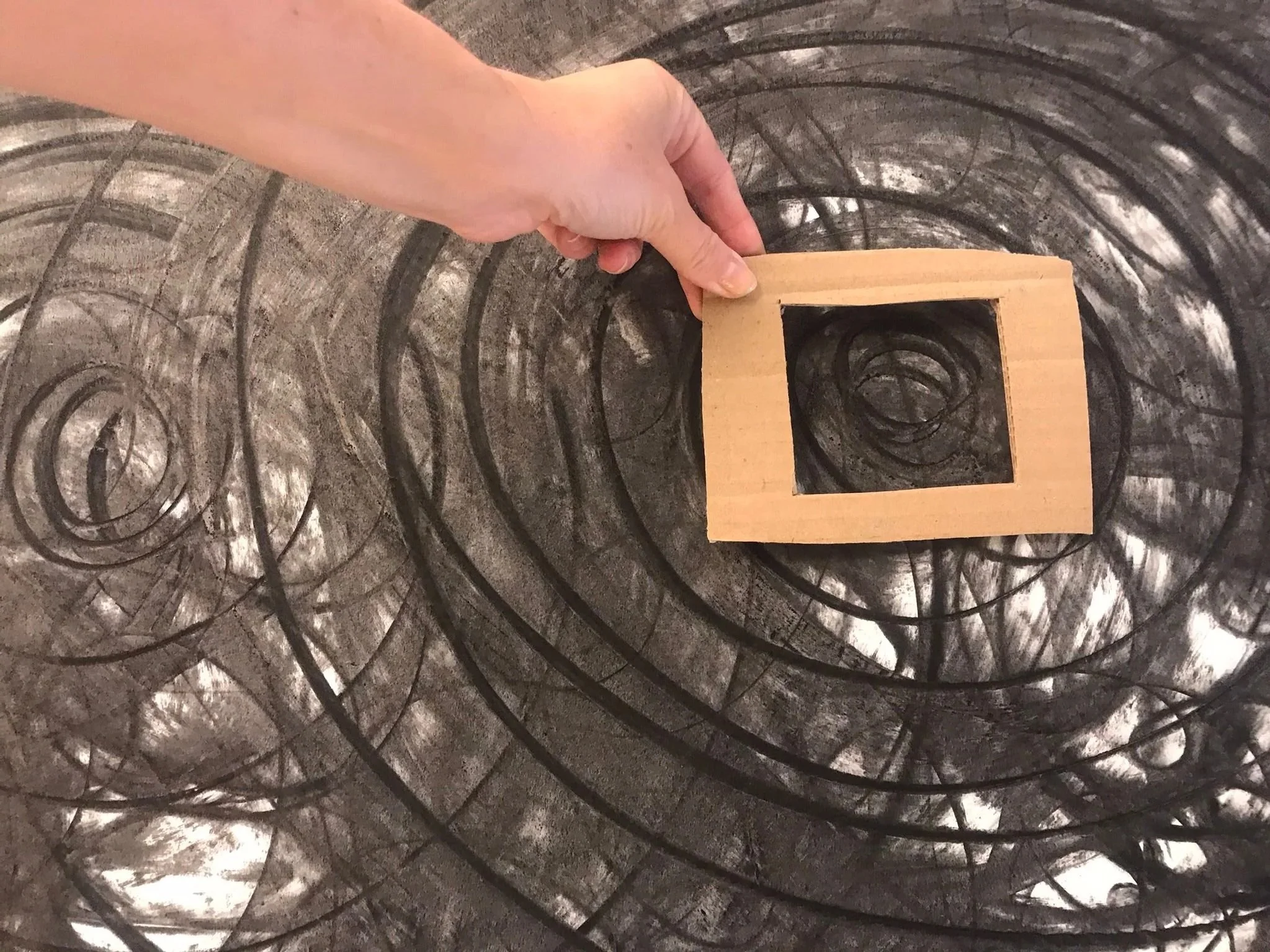 Une personne tient un cadre en bois dans un tunnel sombre et créatif, entouré de lignes noires en spirale sur les murs.