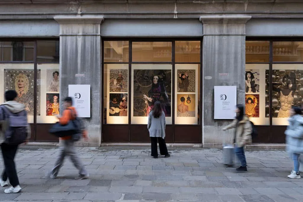 People walking past an art gallery window display on a city street with large photographs and artworks.