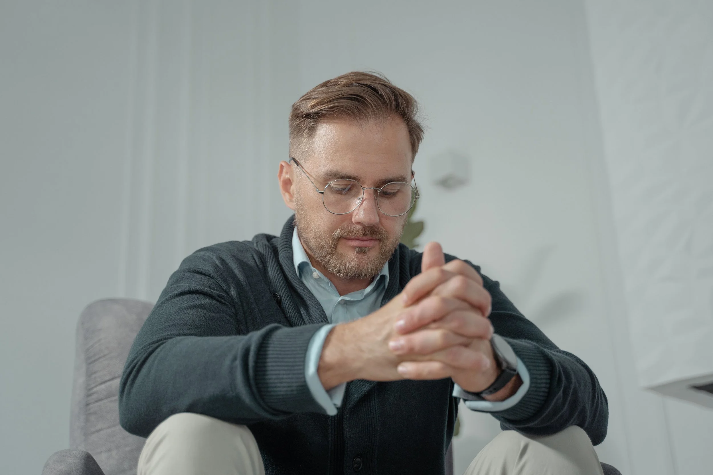 A masculine person with a pensive expression clasping his hands