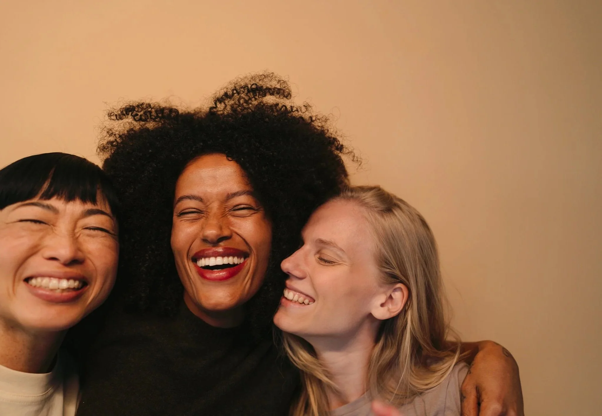 Close-up of four women smiling and hugging in a group, with three of them showing happy, joyful expressions.