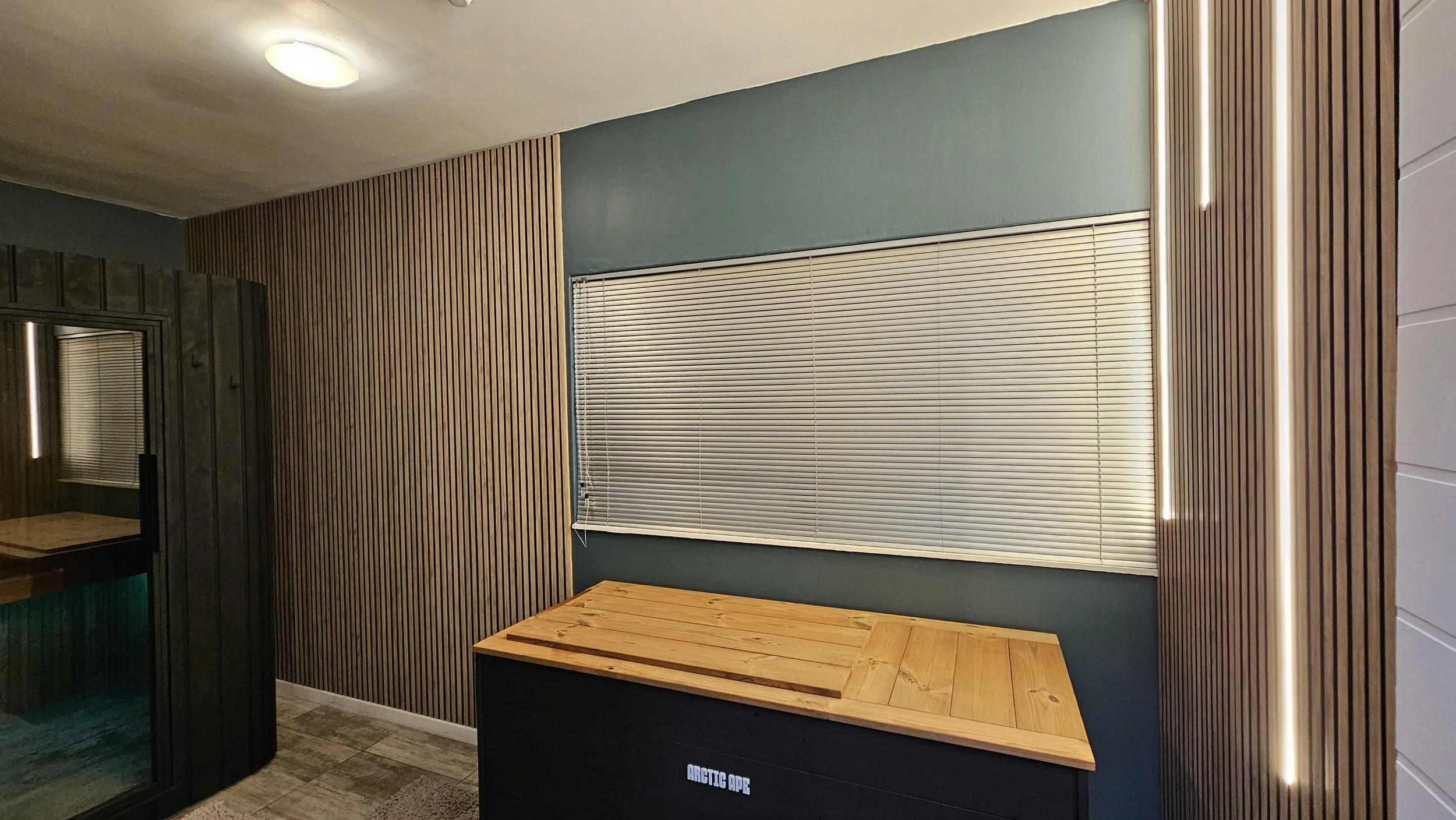 Interior room with wood-paneled walls, closed blinds on a window, a wooden bench, and a ceiling light.