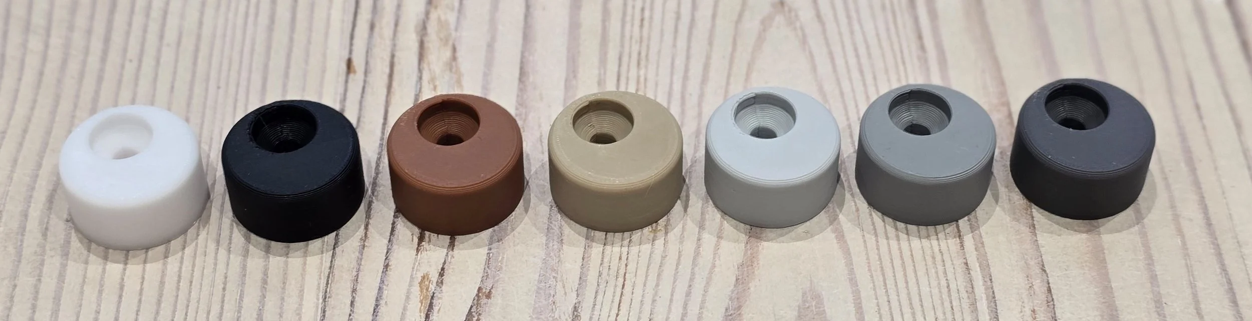 All 7 door stop colours lined up together: White, Black, Brown, Wood Effect, Light Grey, Grey, and Dark Grey